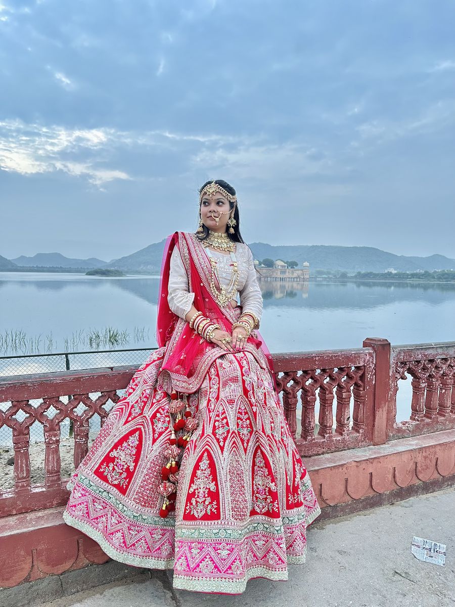 A bride in a red and pink lehenga by the lake at Jal Mahal